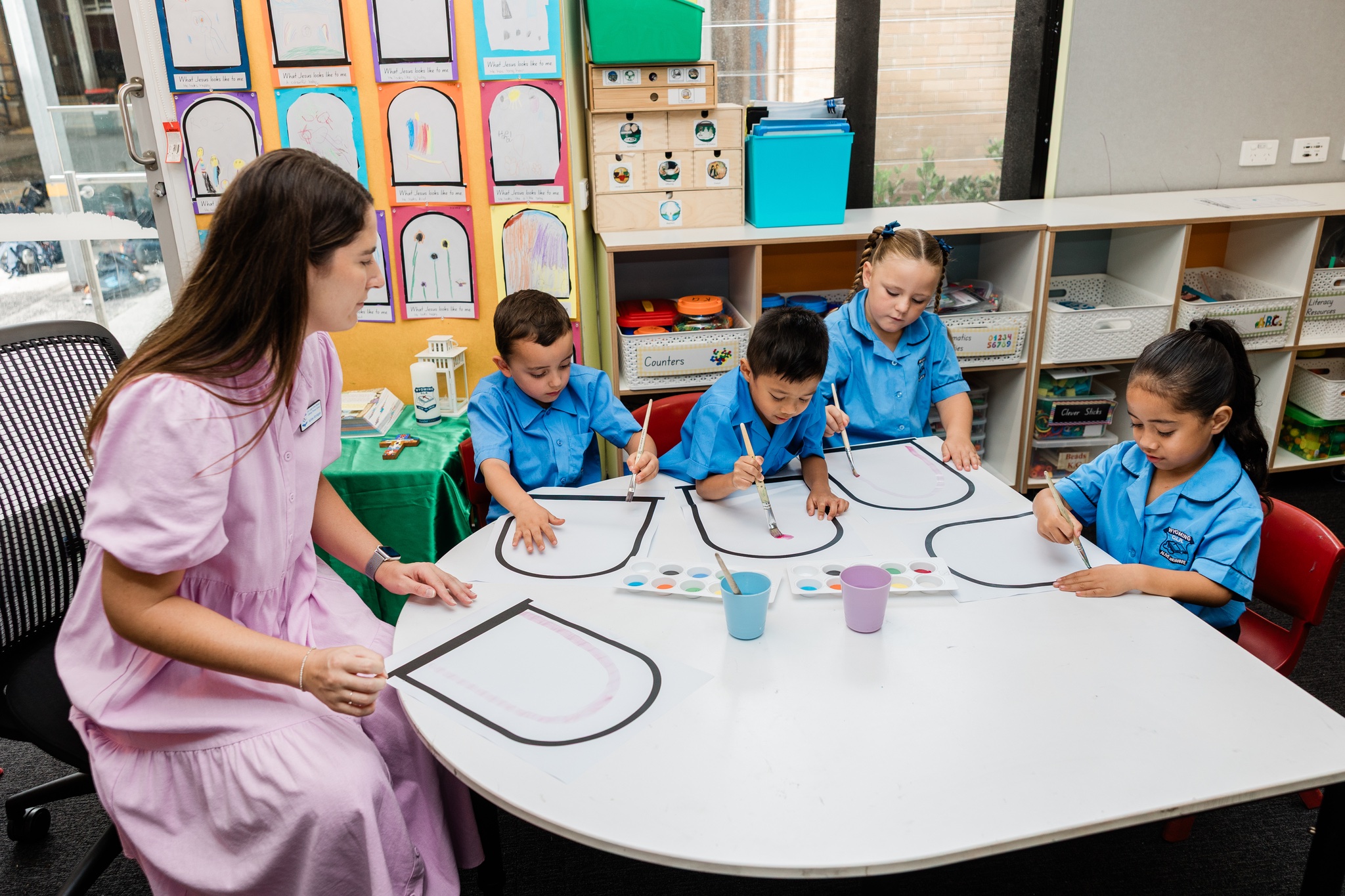 Kindergarten students painting with their teacher during a creative classroom activity